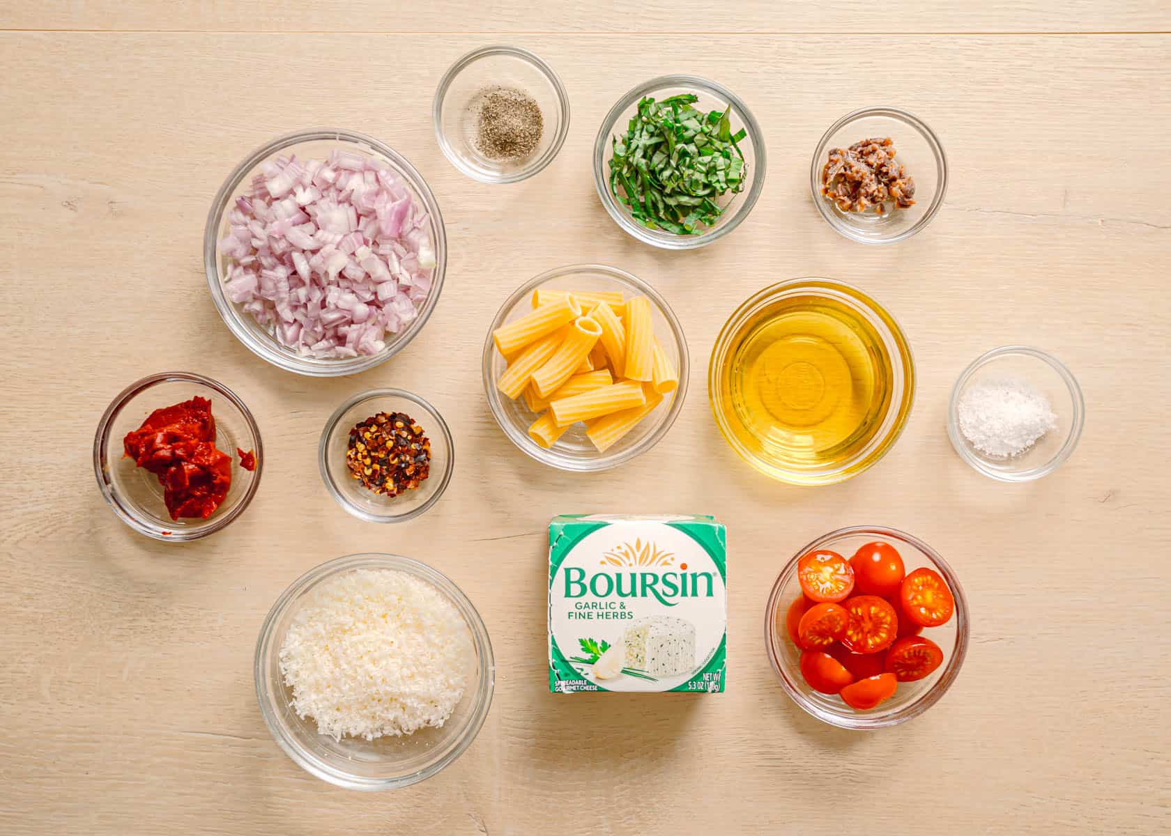 Boursin garlic cheese, rigatoni pasta, cherry tomatoes, tomato paste, olive oil, and shallots arranged on a tabletop for baked Boursin tomato pasta.