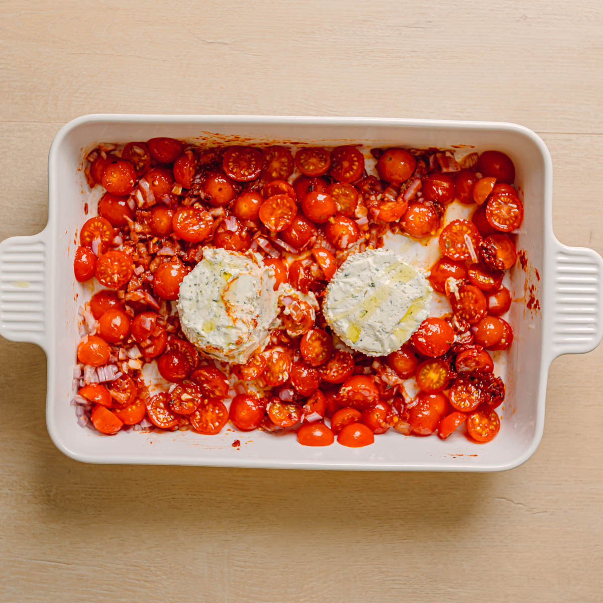 cherry tomatoes tossed in olive oil and tomato paste mixture in baking dish with Boursin cheese placed in center.