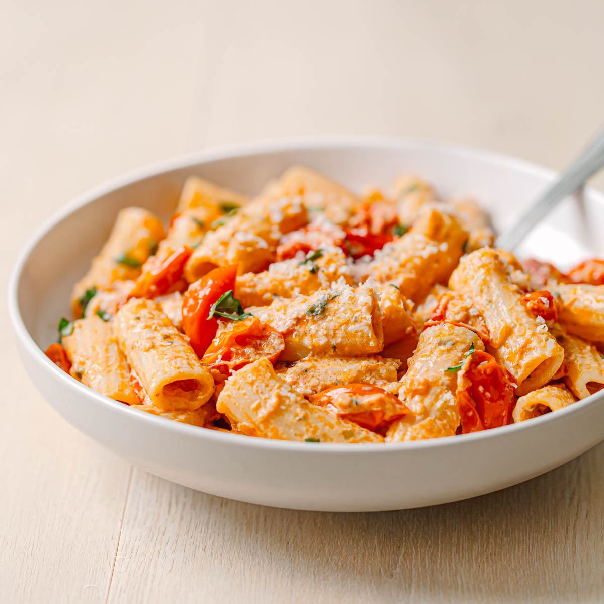 Delicious Boursin tomato pasta. Rigatoni pasta with roasted cherry tomatoes and Boursin cheese in ceramic serving bowl.