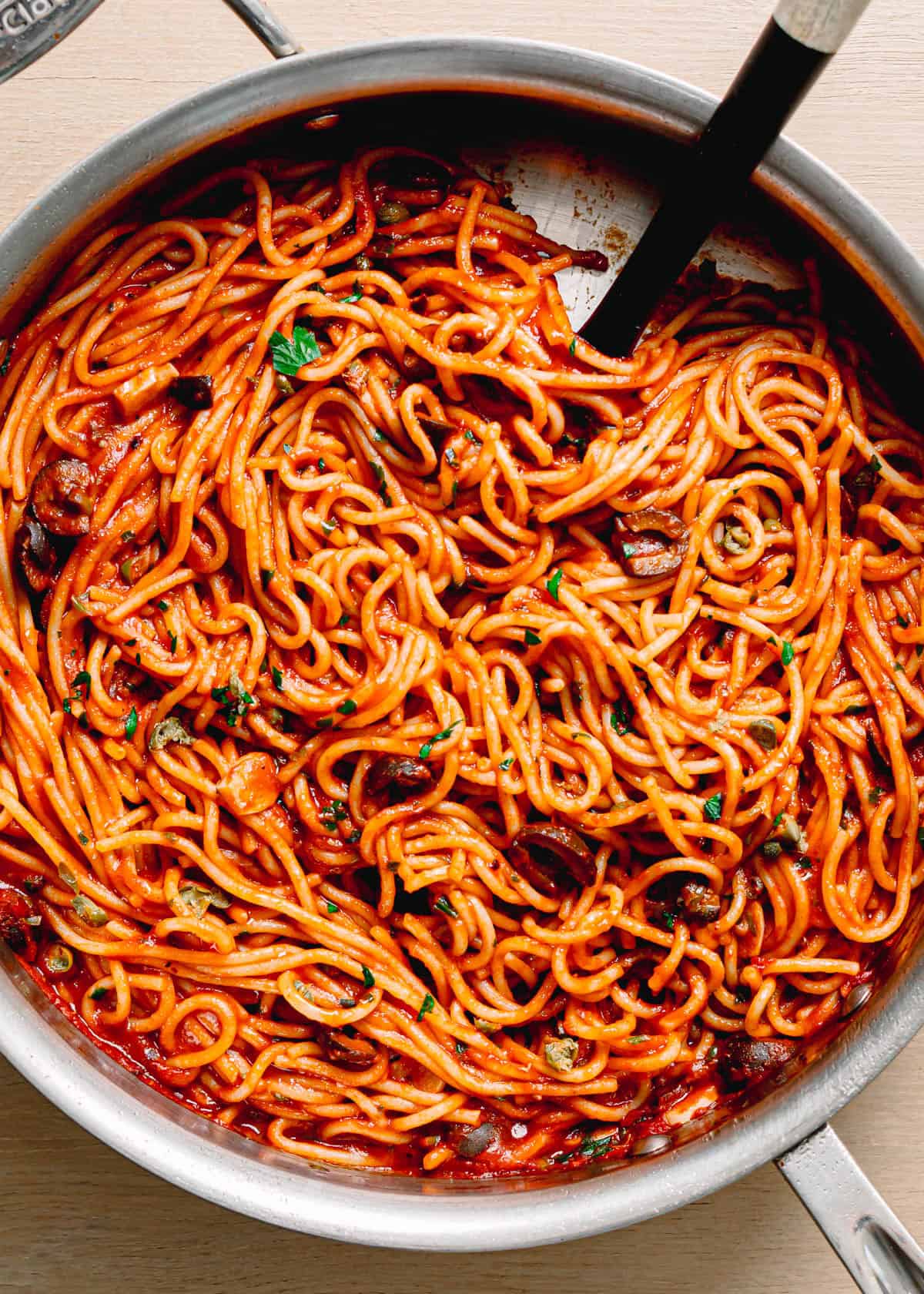 Easy pasta puttanesca recipe served in a large skillet with spaghetti, crushed tomatoes, olives, capers, anchovy fillets and fresh parsley.