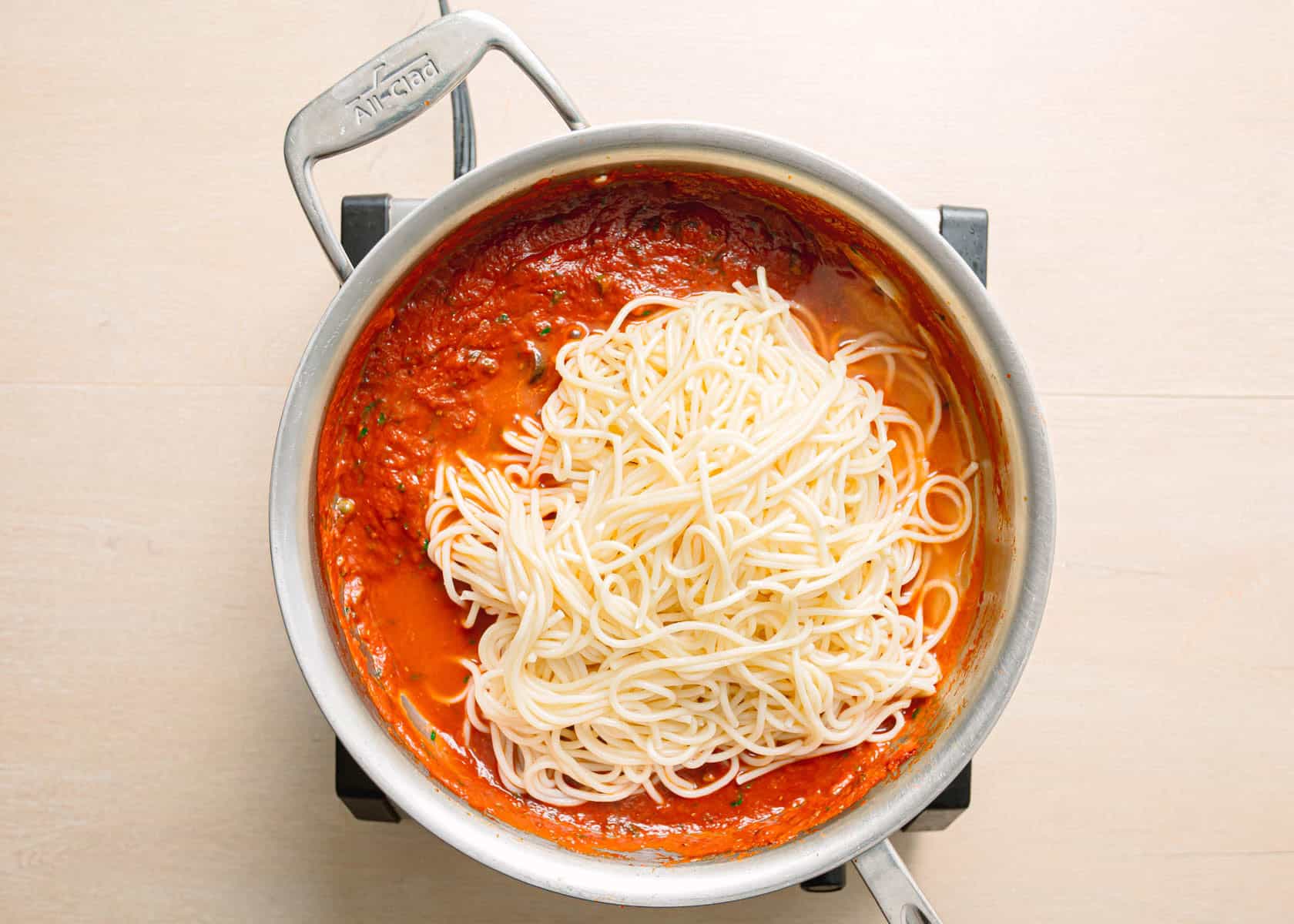 Tossing cooked spaghetti in puttanesca sauce in a skillet for easy pasta puttanesca recipe.