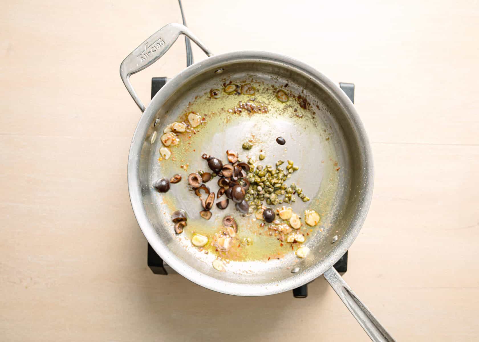Adding capers and olives to skillet for easy pasta puttanesca recipe.
