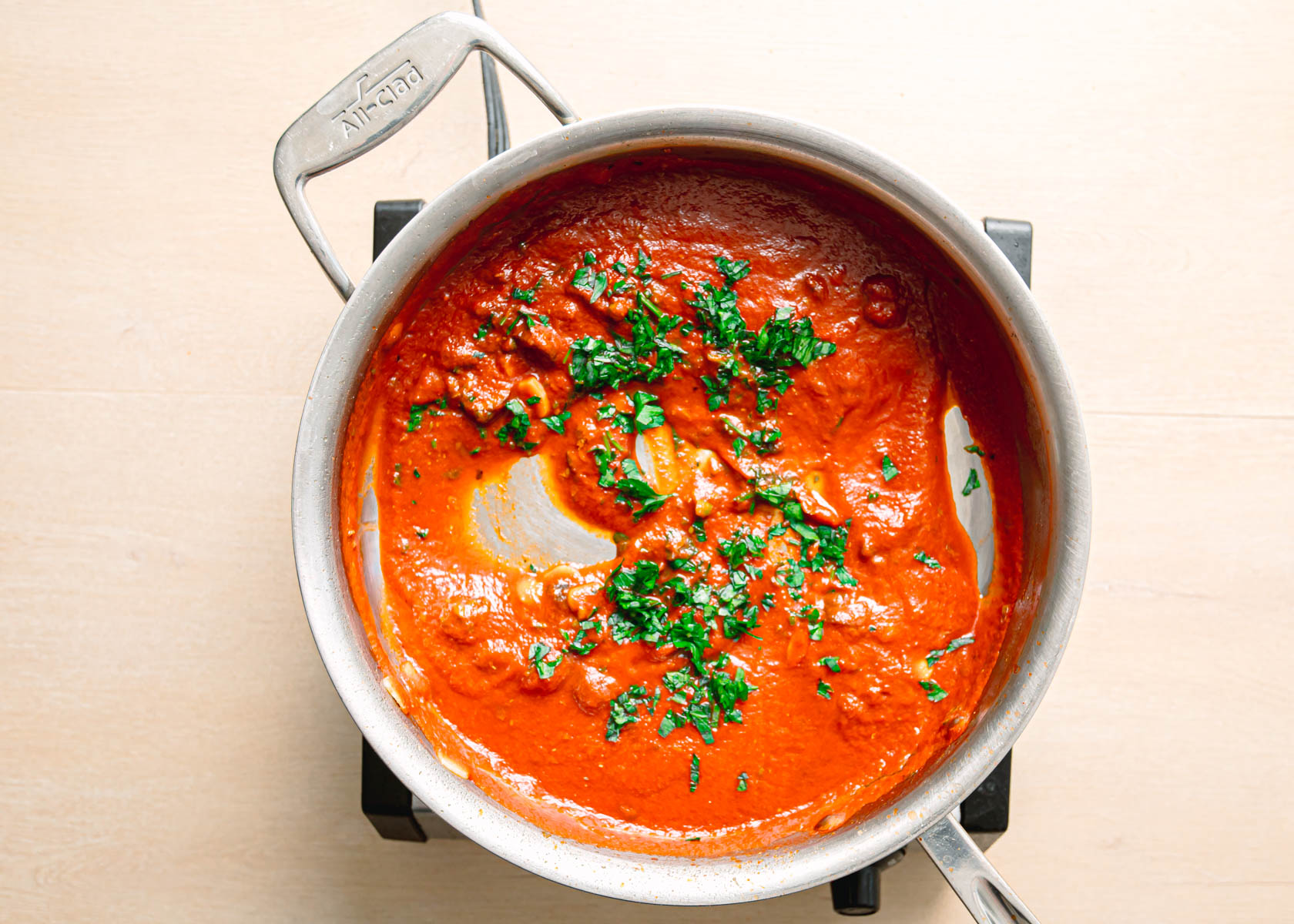 Pouring crushed tomatoes and fresh parsley into skillet for pasta puttanesca recipe.