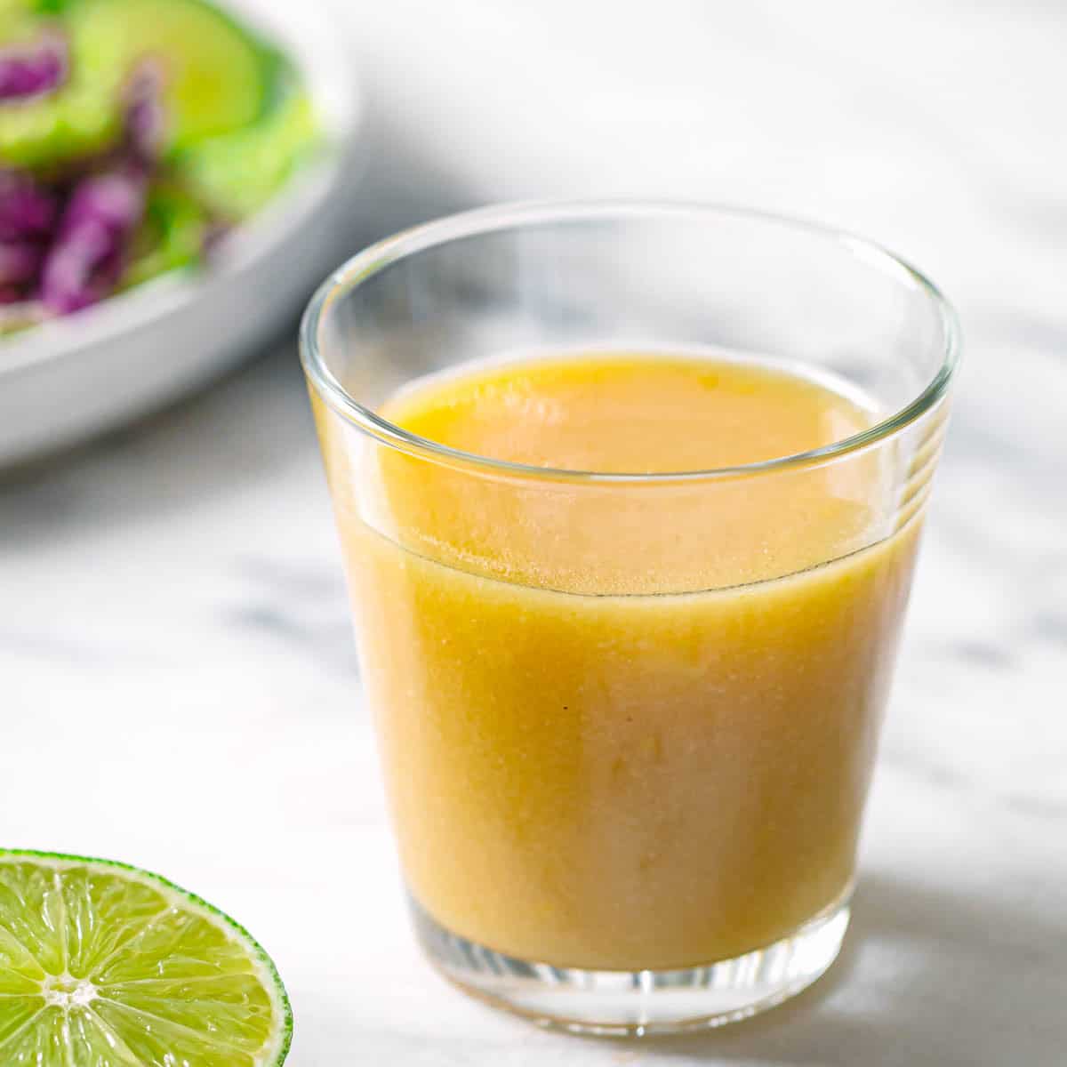 Easy homemade miso salad dressing served in a clear glass cup with fresh lime on a marble surface.