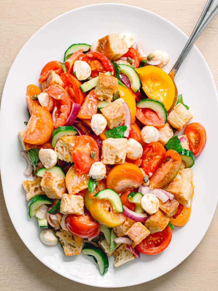 Easy panzanella salad recipe served in an oval bowl with heirloom tomatoes mozzarella balls fresh basil and toasted ciabatta.