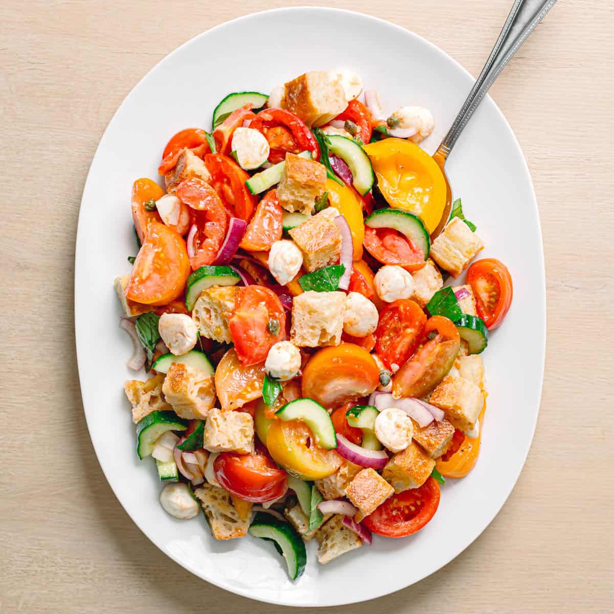 Easy panzanella salad recipe served in an oval bowl with heirloom tomatoes mozzarella balls fresh basil and toasted ciabatta.