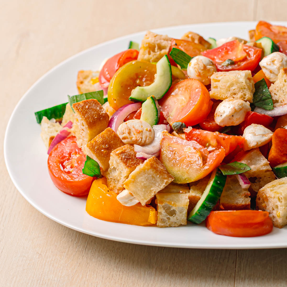 Easy panzanella salad recipe ready to serve in an oval bowl from the side with colorful heirloom tomatoes and golden bread.