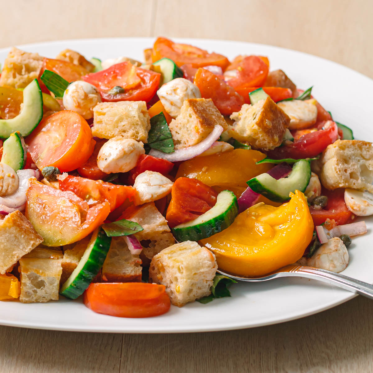 Easy panzanella salad recipe close up side view with soaked ciabatta mozzarella balls and glistening heirloom tomatoes.