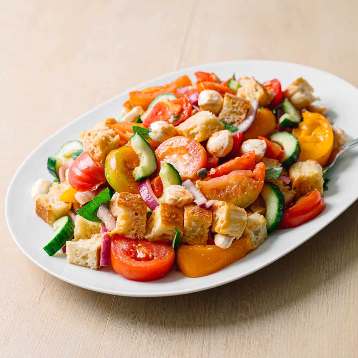 Easy panzanella salad recipe served in an oval bowl from the side on a wooden table with rustic styling.