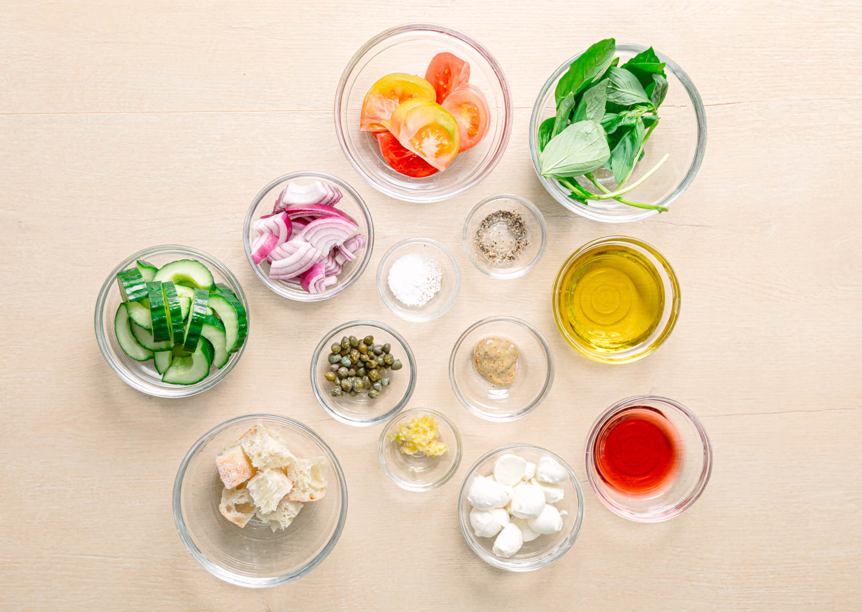 Easy panzanella salad recipe ingredients laid out on a table including ciabatta tomatoes mozzarella balls cucumber red onion and fresh basil.