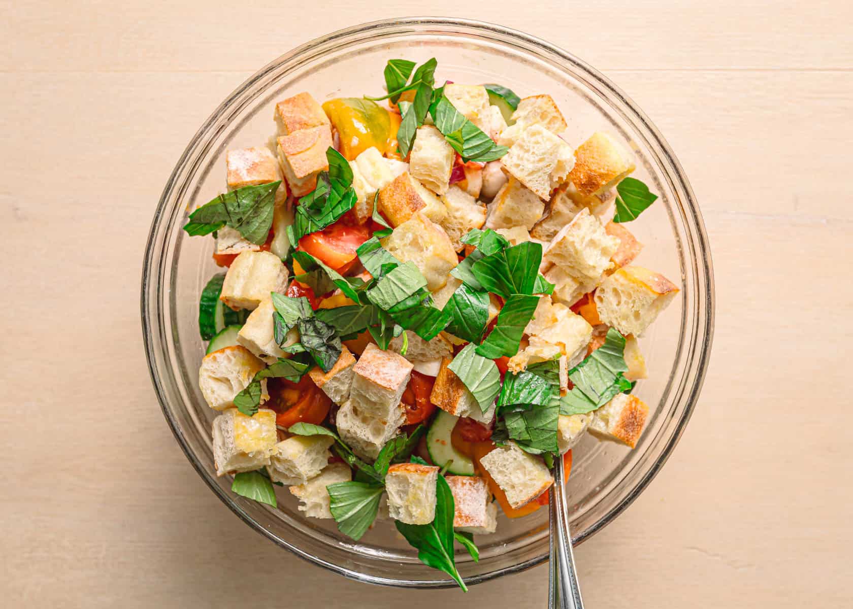 Easy panzanella salad recipe tossing toasted ciabatta tomatoes cucumber mozzarella and basil in a large bowl.