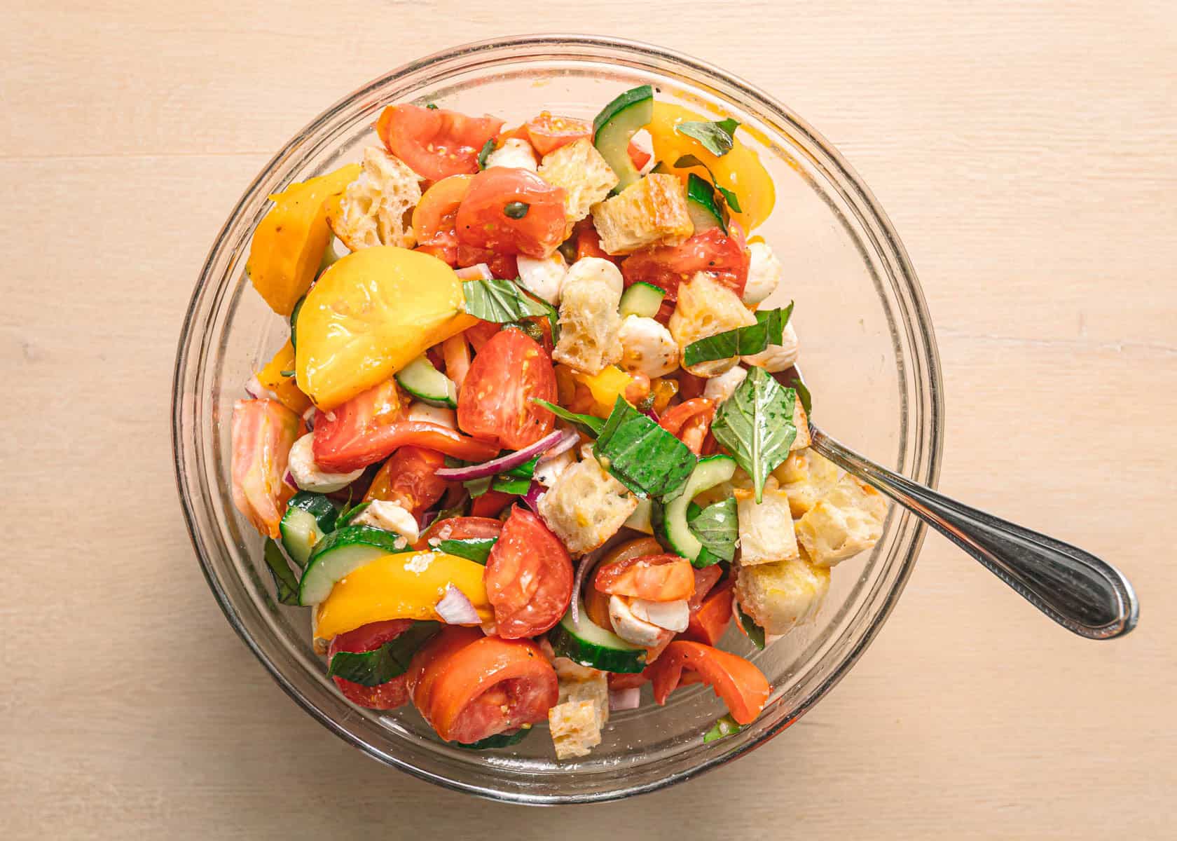 Easy panzanella salad recipe served at room temperature with fresh basil and mozzarella on top.