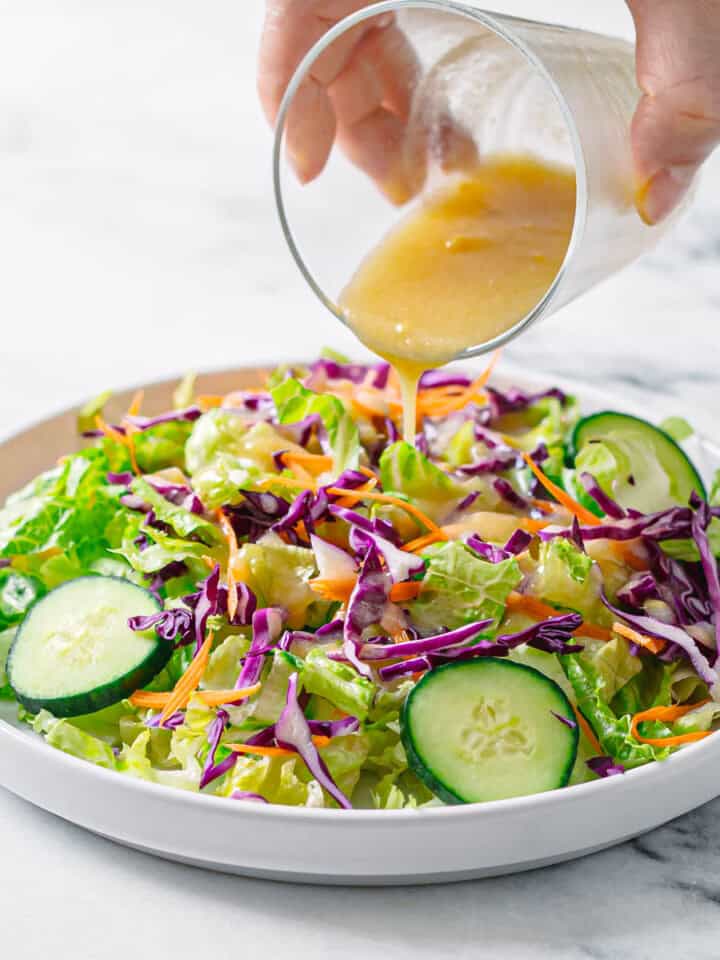 Homemade miso salad dressing being poured over fresh green salad with cabbage and cucumber.