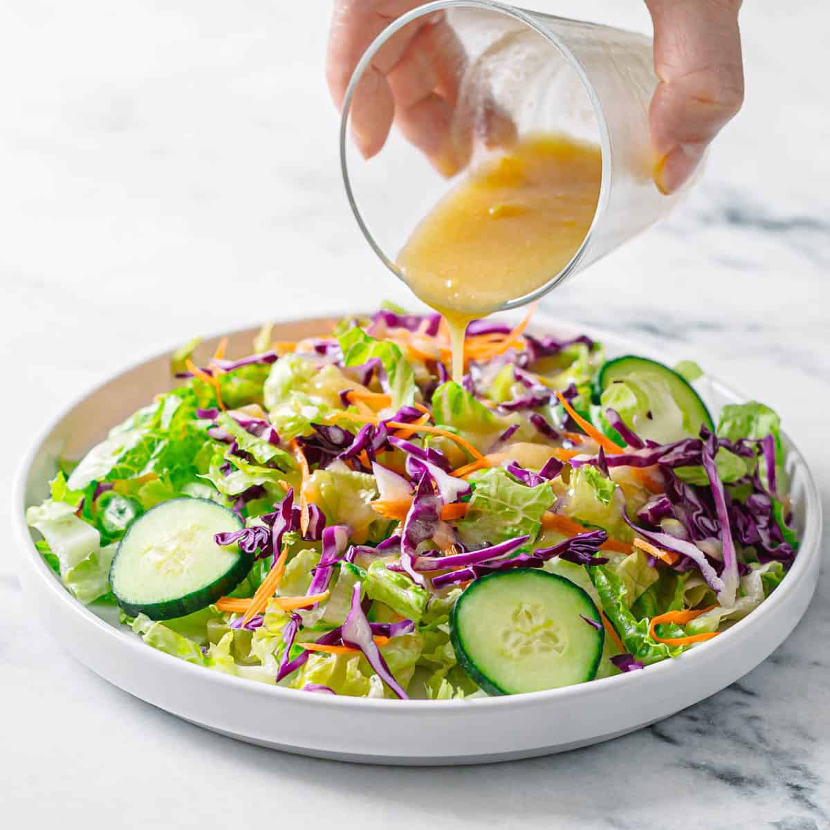 Homemade miso salad dressing being poured over fresh green salad with cabbage and cucumber.