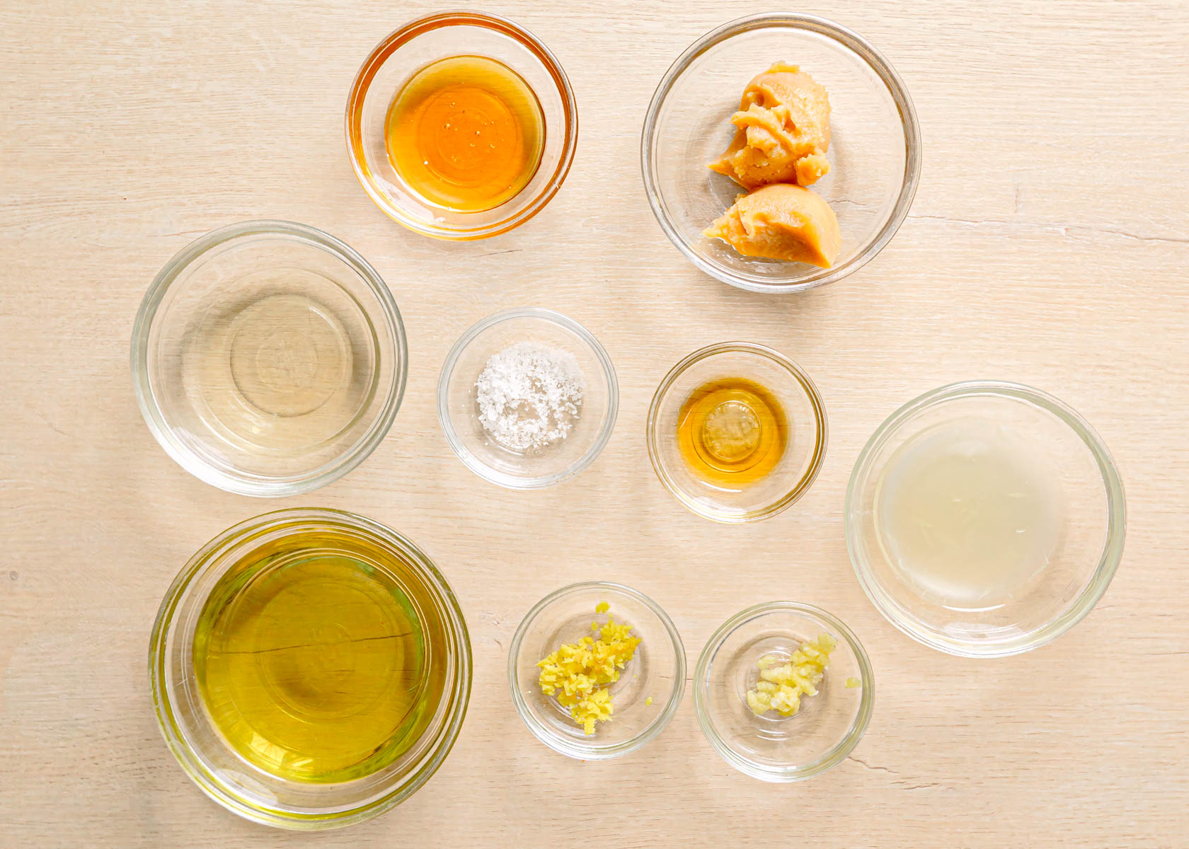 White miso salad dressing ingredients flatlay including avocado oil, honey, garlic, lime, ginger, and sesame oil.