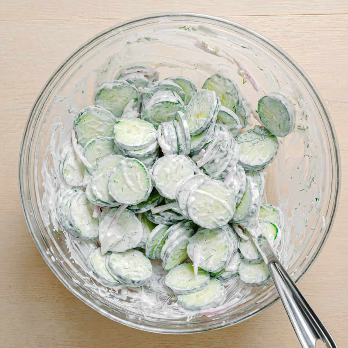 Tossing cucumber dill salad together in a bowl.