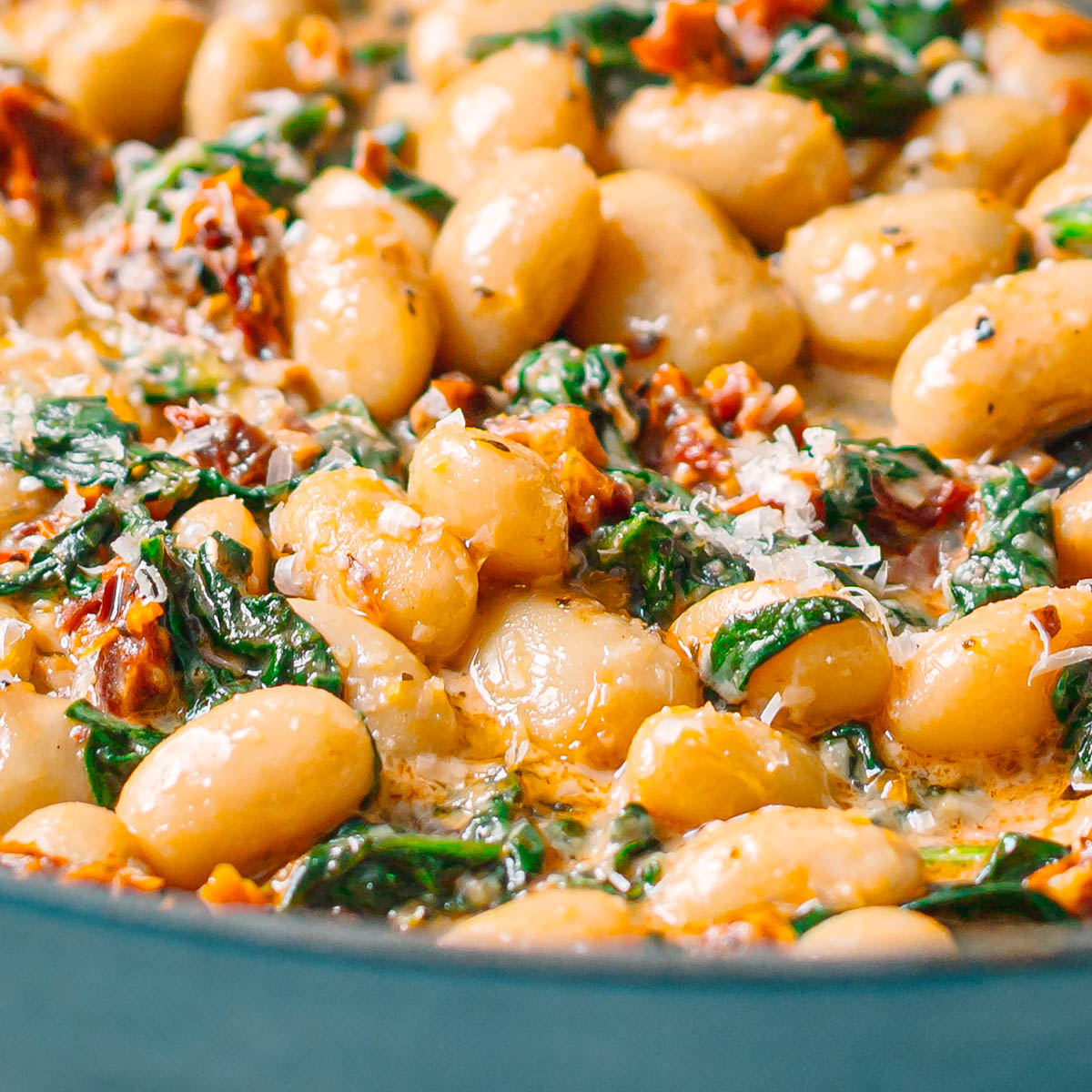 Close up side view of creamy marry me butter beans, showing the thick sauce, spinach, and melted parmesan.