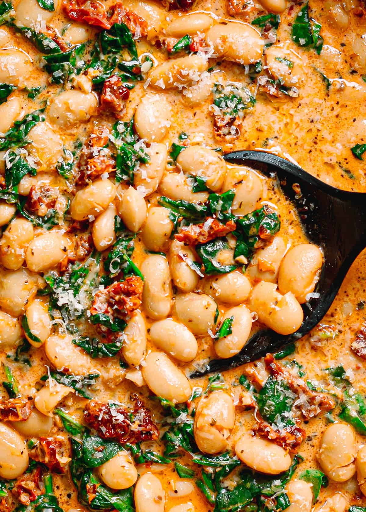 Close up of creamy marry me butter beans showing melted parmesan and sun dried tomatoes.