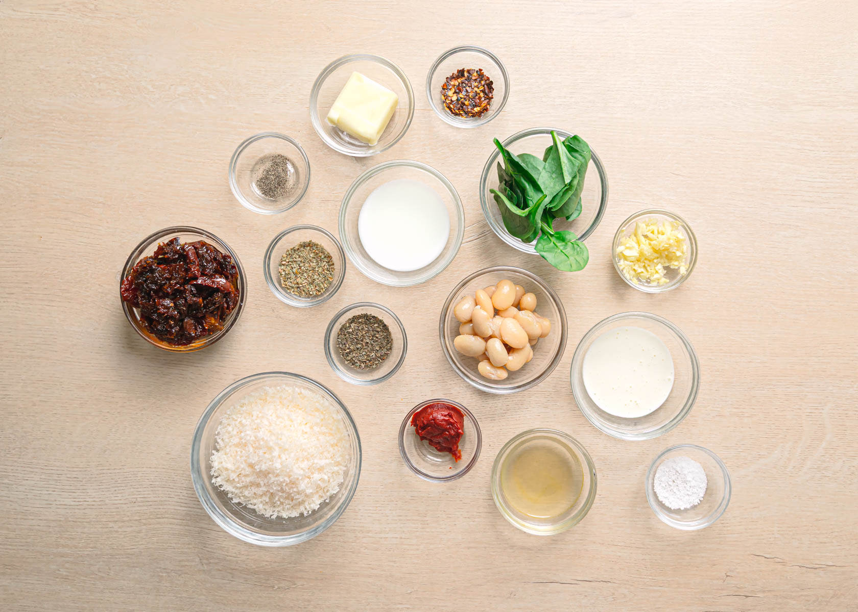 Ingredients for marry me butter beans laid out on a table, including canned butter beans, sun dried tomatoes, garlic, and parmesan cheese.