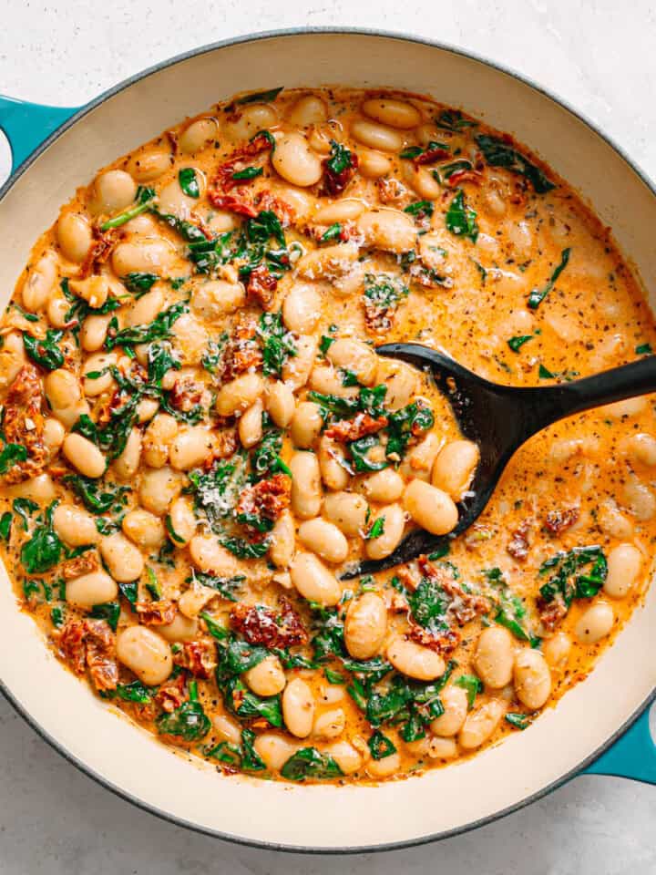 Creamy white bean stew with spinach and herbs in a blue skillet.