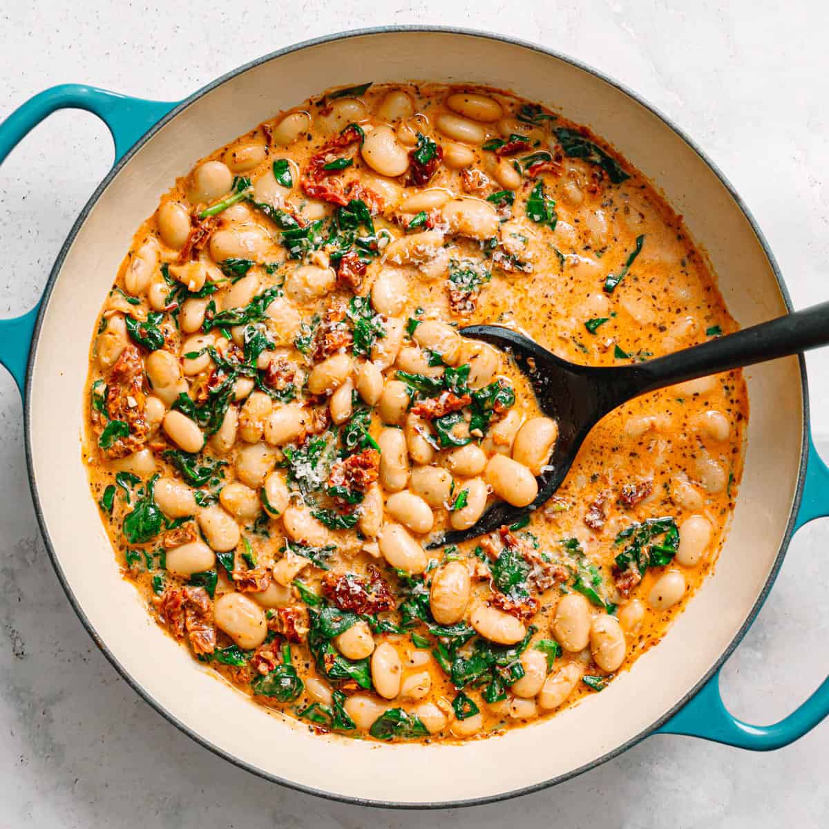 Creamy white bean stew with spinach and herbs in a blue skillet.