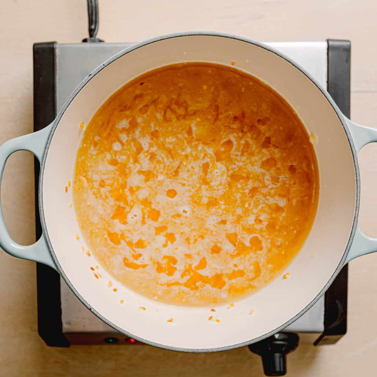 Pouring chicken broth over orzo in a pot.