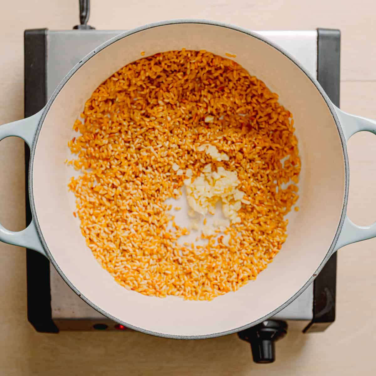 Adding minced garlic to toasted orzo.