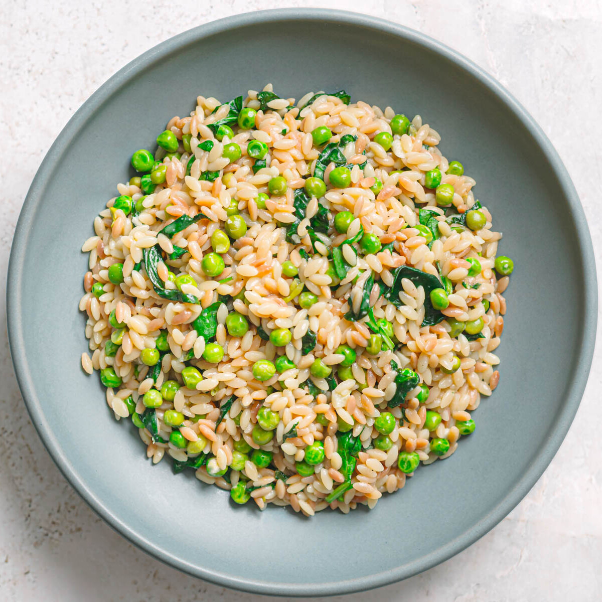 Bowl of orzo with peas and spinach, top view.
