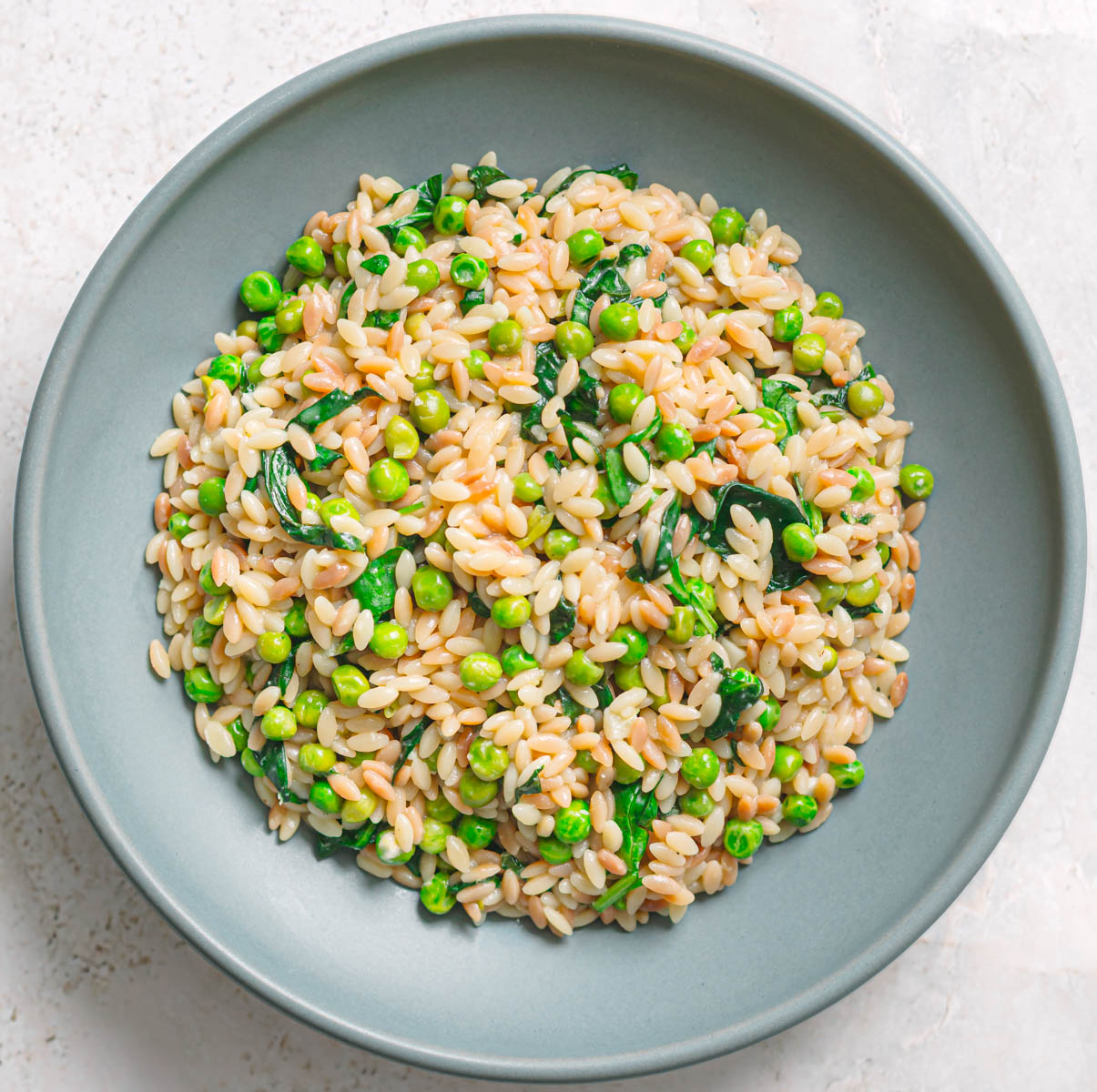 Bowl of orzo with peas and spinach, top view.
