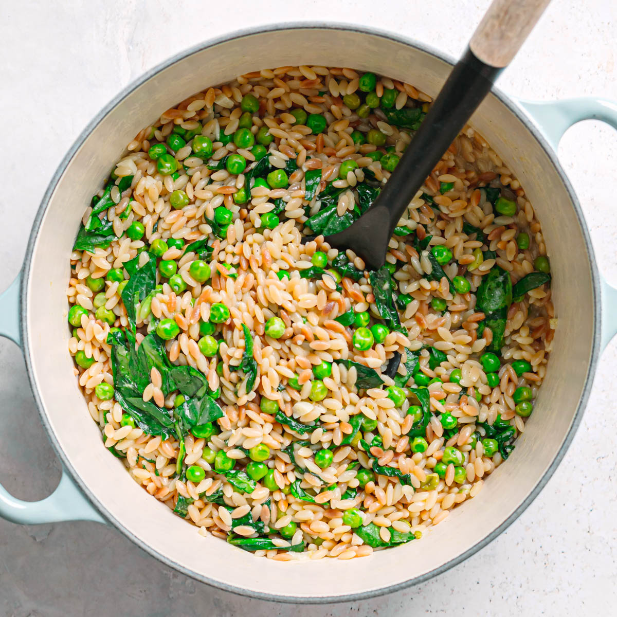 Top view of orzo with peas and spinach in a pot.