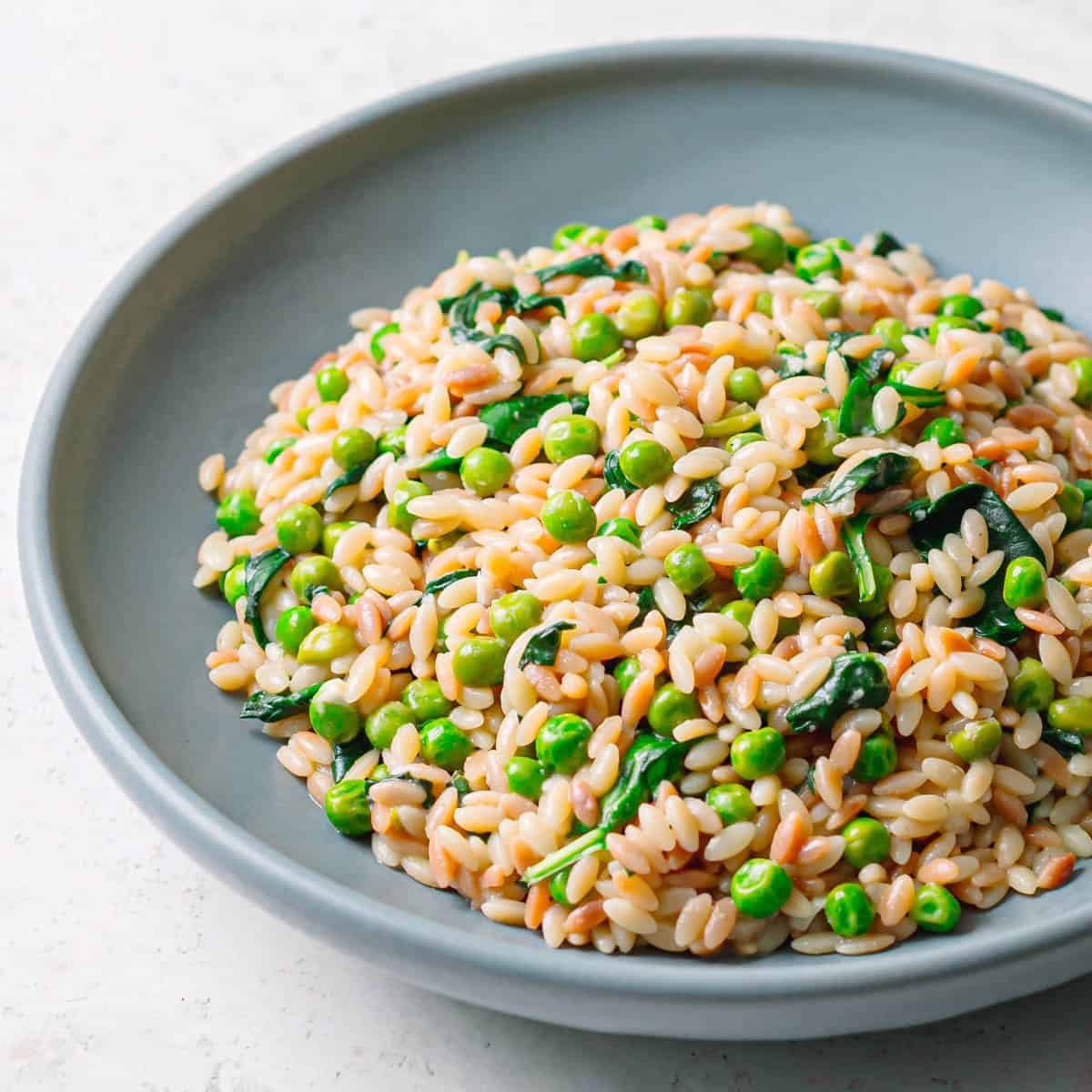 Side view of orzo with peas and spinach in a bowl.