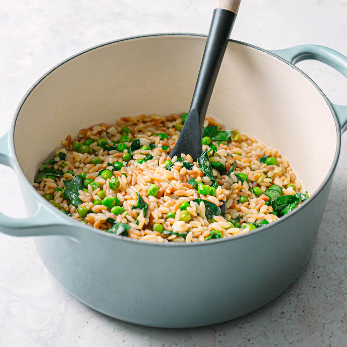Side view of orzo with peas cooking in a pot.